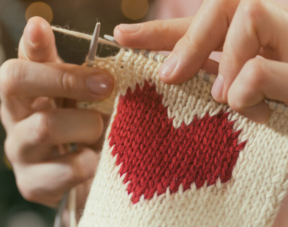 Concept of love and concern. Woman knitting the red heart for her loved one. Valentines postcard.
